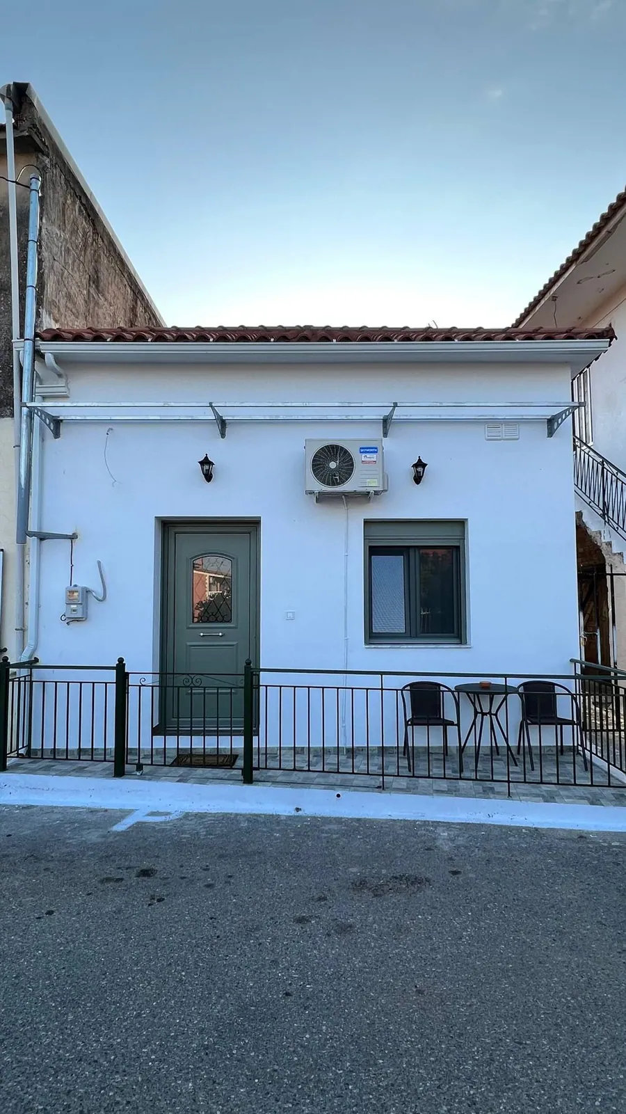 Η λευκή πρόσοψη του σπιτιού με την πράσινη πόρτα και το κλιματιστικό