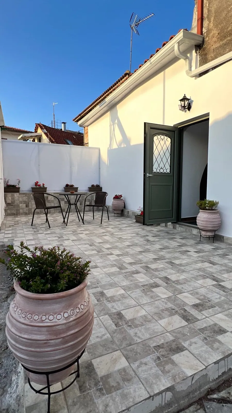 Πλακόστρωτη αυλή με γλάστρες και την πράσινη πόρτα του σπιτιού