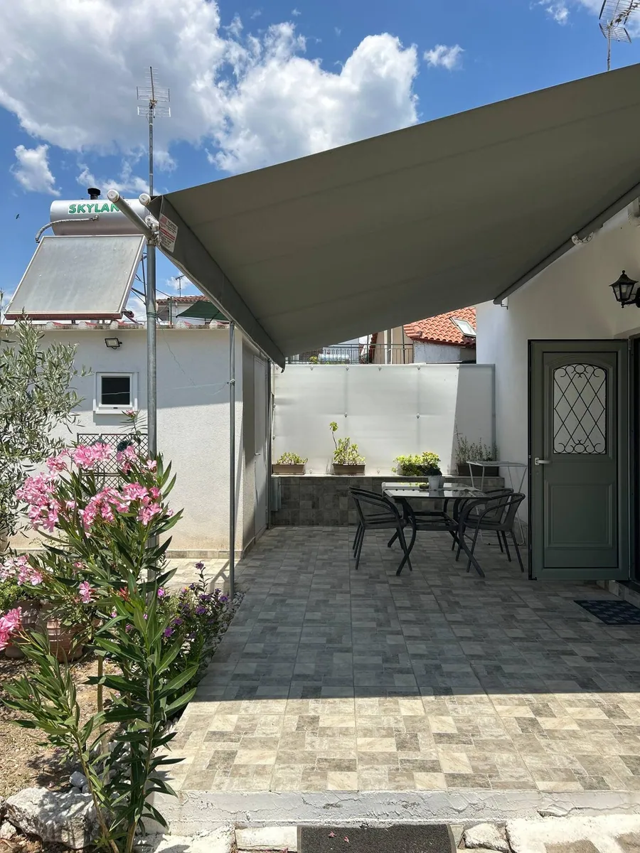 Η βεράντα με την τέντα, ένα τραπέζι με καρέκλες και πικροδάφνες δίπλα